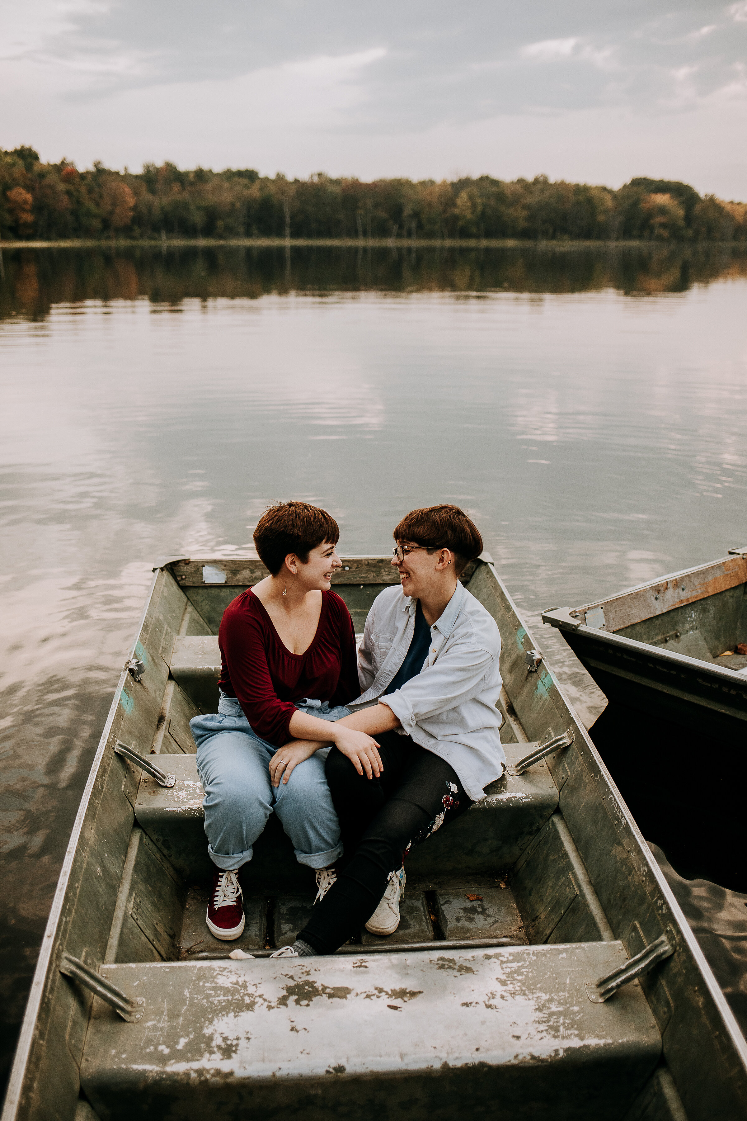  Beautiful couple in a boat by the dock on a lake wearing maroon and gray in this engagement photoshoot by Kindred + Co in Indiana. boat photoshoot dock by lake photoshoot indiana fort wayne engagement photoshoot locations maroon and gray same-sex co
