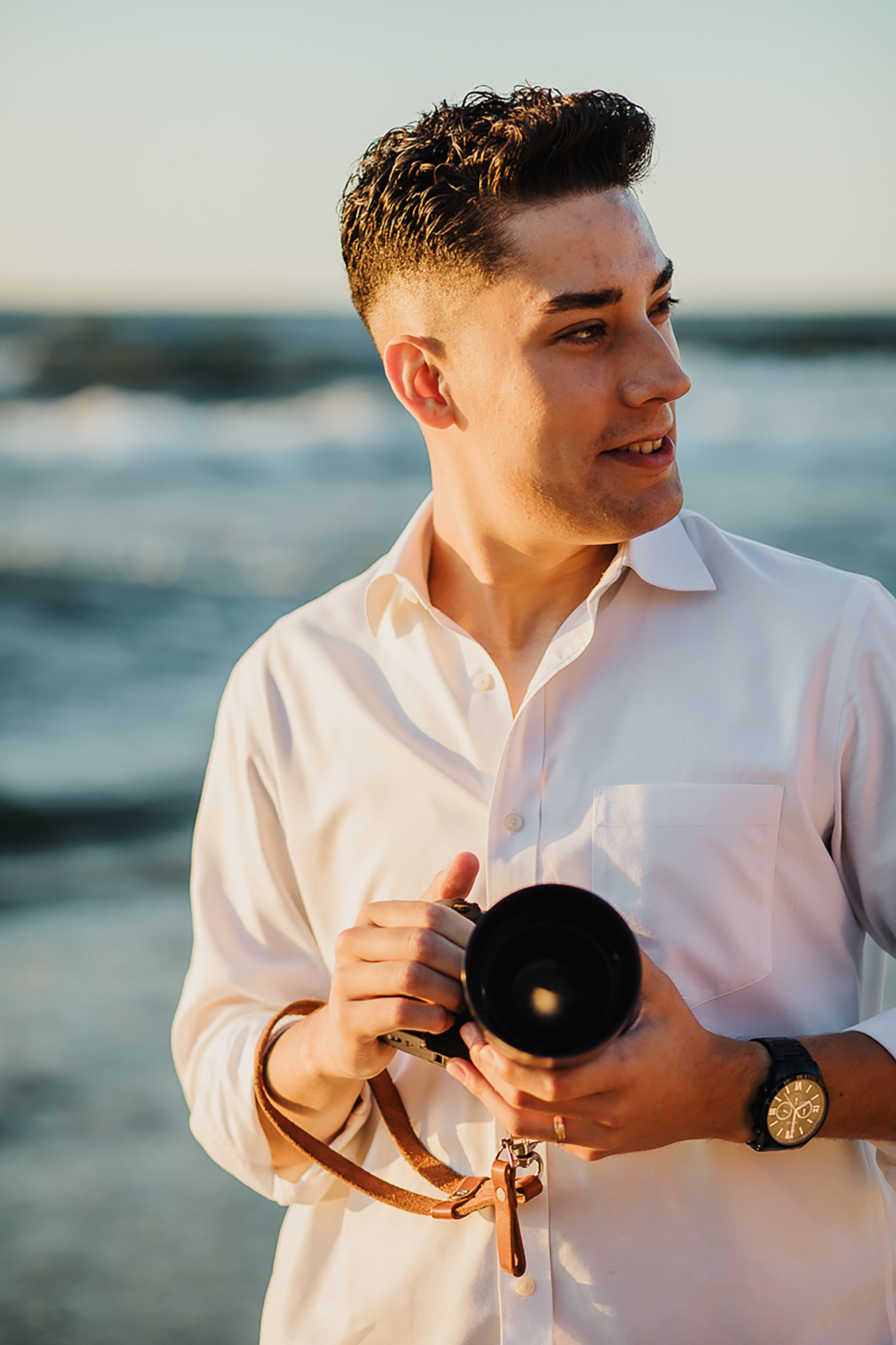  Wedding portraits of groom on the lakeshore by Kindred &amp; Co. Photography at Indiana Dunes National Lakeshore. casual groom elopement attire, groom rolled up sleeved button up white shirt, groom holding dsr camera, leather dsr camera strap, profe