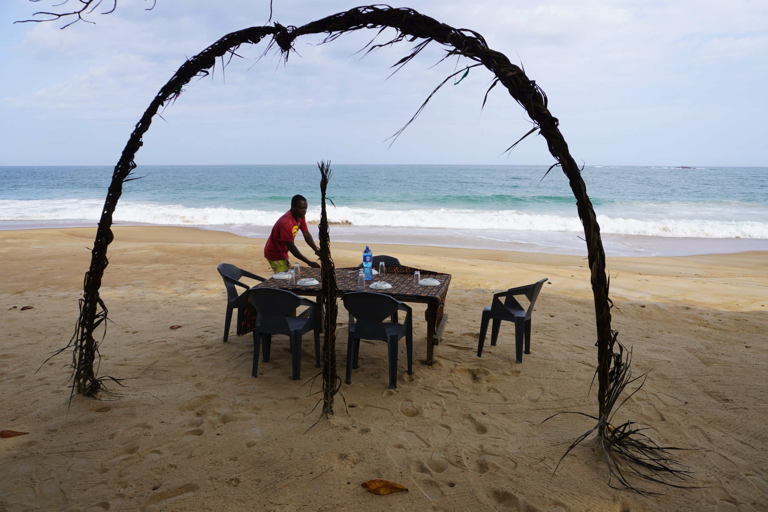  Sur la plage de Roc, a deux pas de l’écolodge, Prince Douh, musicien et cuisinier, met la table pour les invités d’aujourd’hui. Il a préparé du poulet sauce tomate et de la noix de palmier avec du riz blanc.  