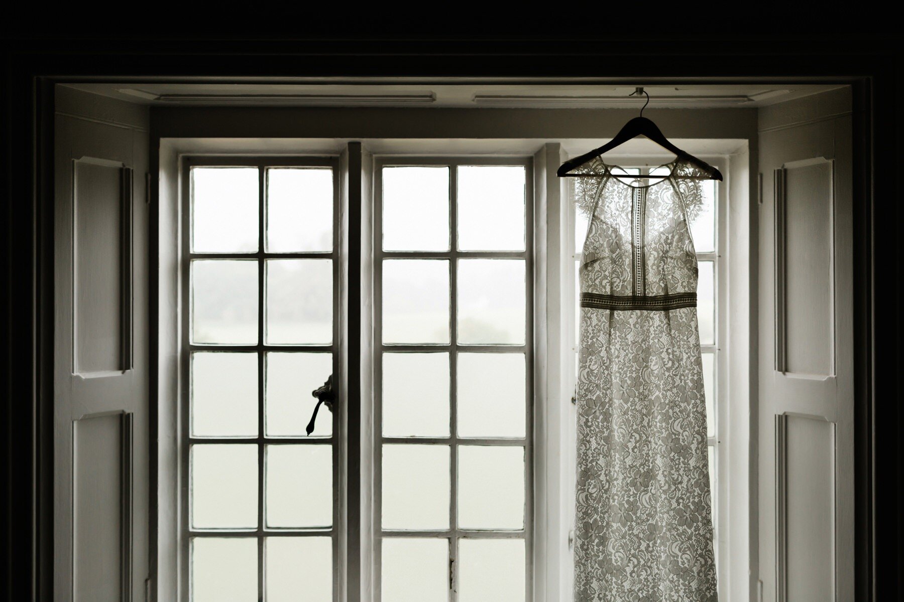 A vintage wedding dress hanging against a window at Horsley Towers wedding venue
