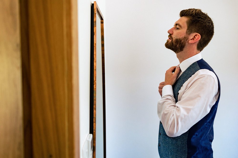 A groom adjusting his tie in the mirror ahead of his wedding