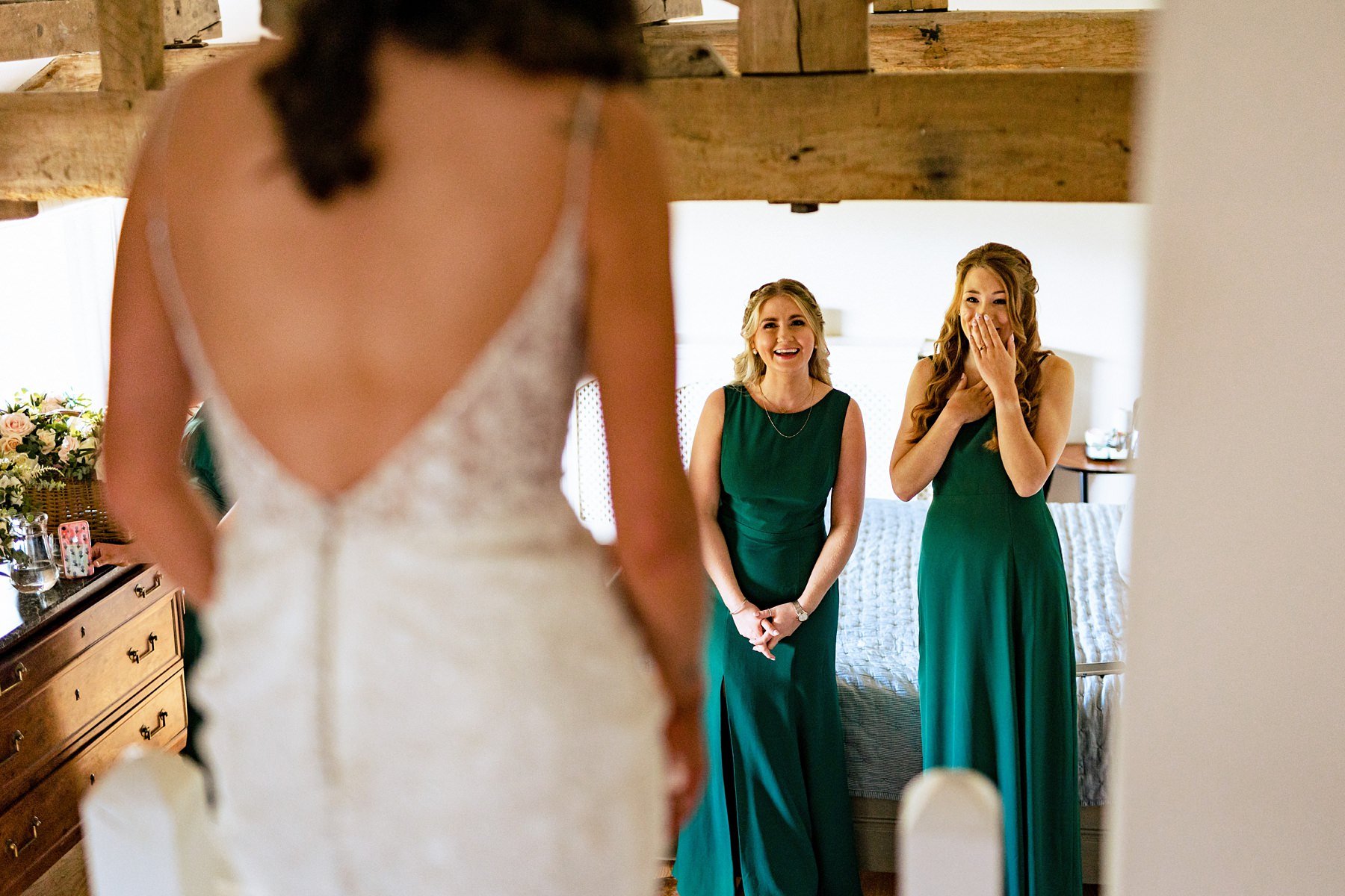 A bridesmaid smiling covering her mouth in excitement as she sees her friend in her wedding dress just before her wedding
