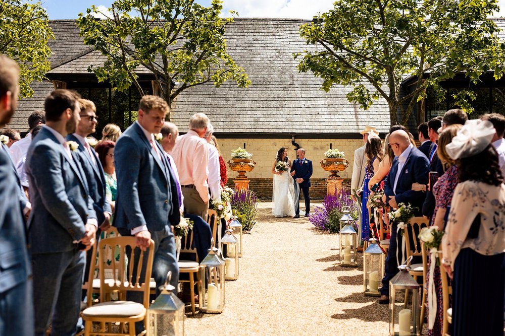 A father walks his daughter down the aisle for an outdoors wedding ceremony at Bury Court Barn 