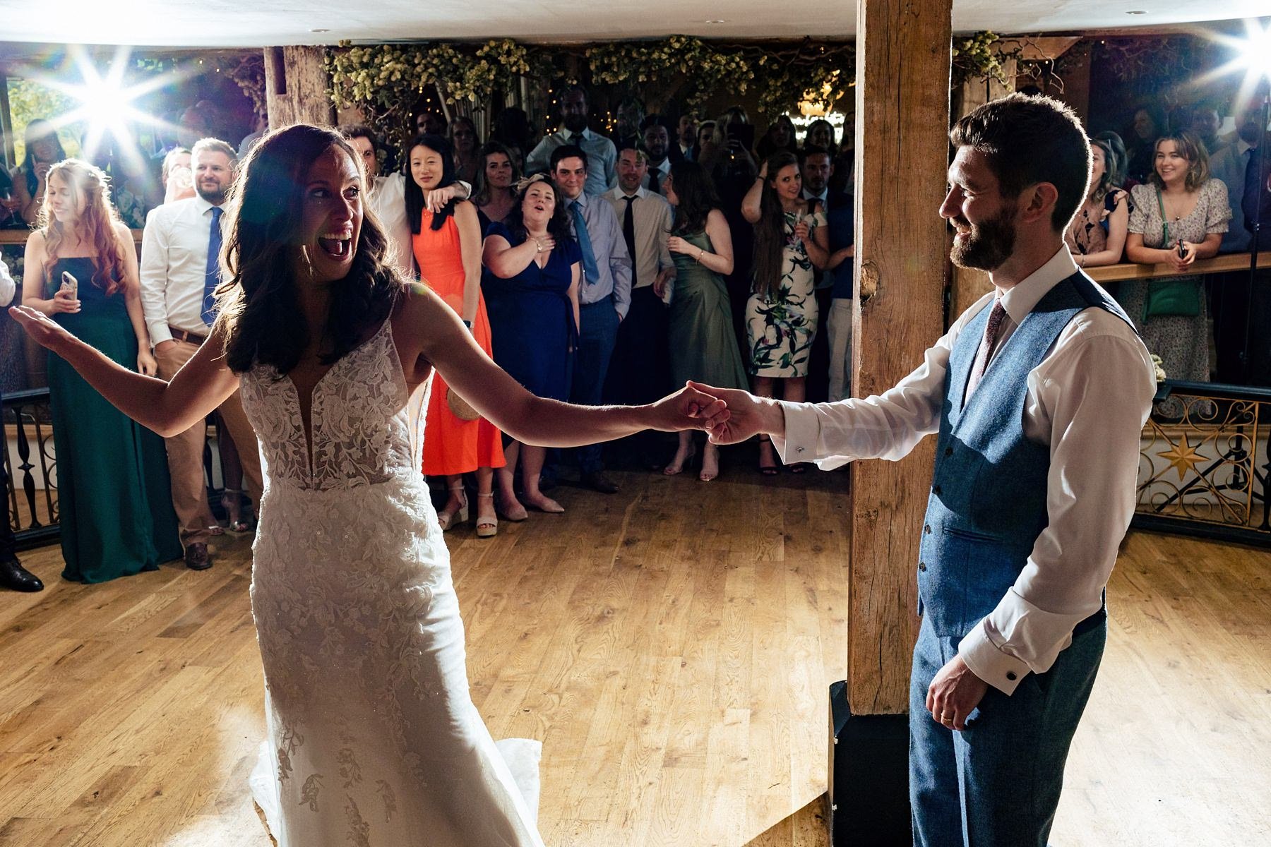 A bride leans back and puts out an arm as she dances with her new husband for their first dance at Bury Court Barn