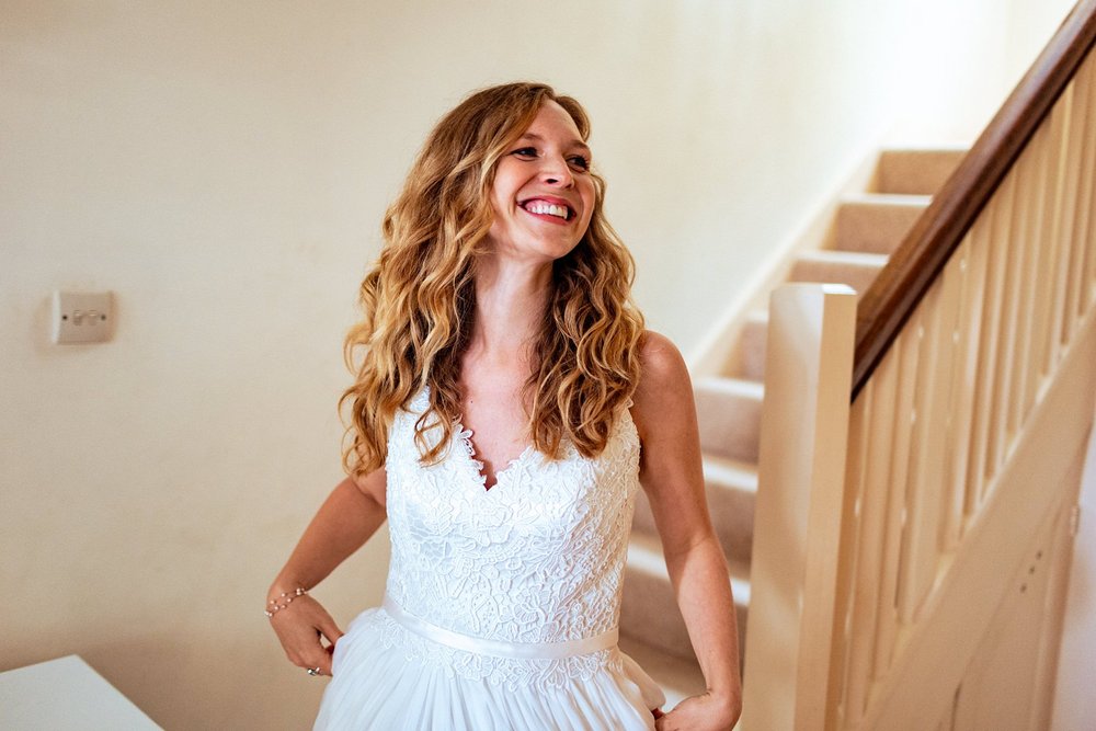A bride beaming with joy as she comes down the stairs in her wedding dress