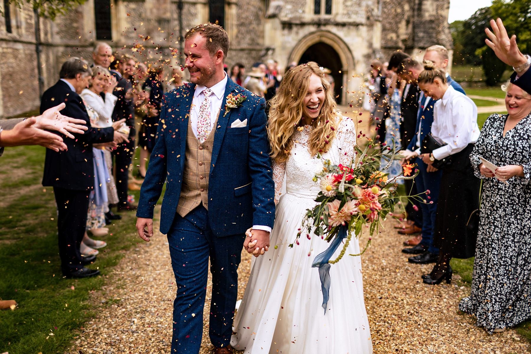 A bride and groom have confetti thrown over them as they leave their wedding