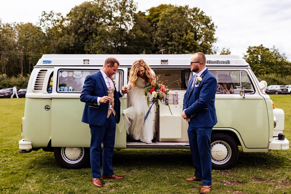 A bride is helped out of a VW campervan at her wedding celebration at Kingsettle Stud