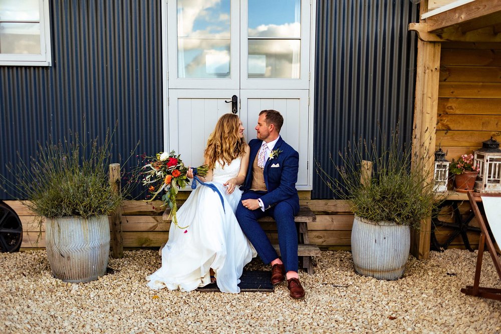 A bride and groom take a seat and hug on the steps of a shepherds hut at Kingsettle Stud