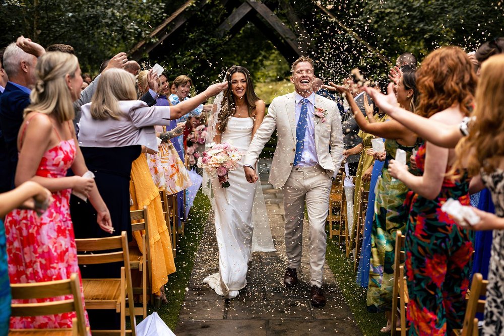 A bride and groom walk back down the aisle at Millbridge Court as their guests shower them in colourful confetti.