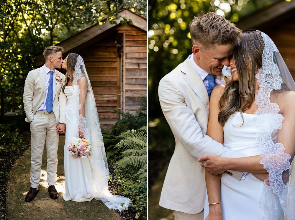 A bride and groom embrace and kiss in front of a wooden cottage at Millbridge Court.
