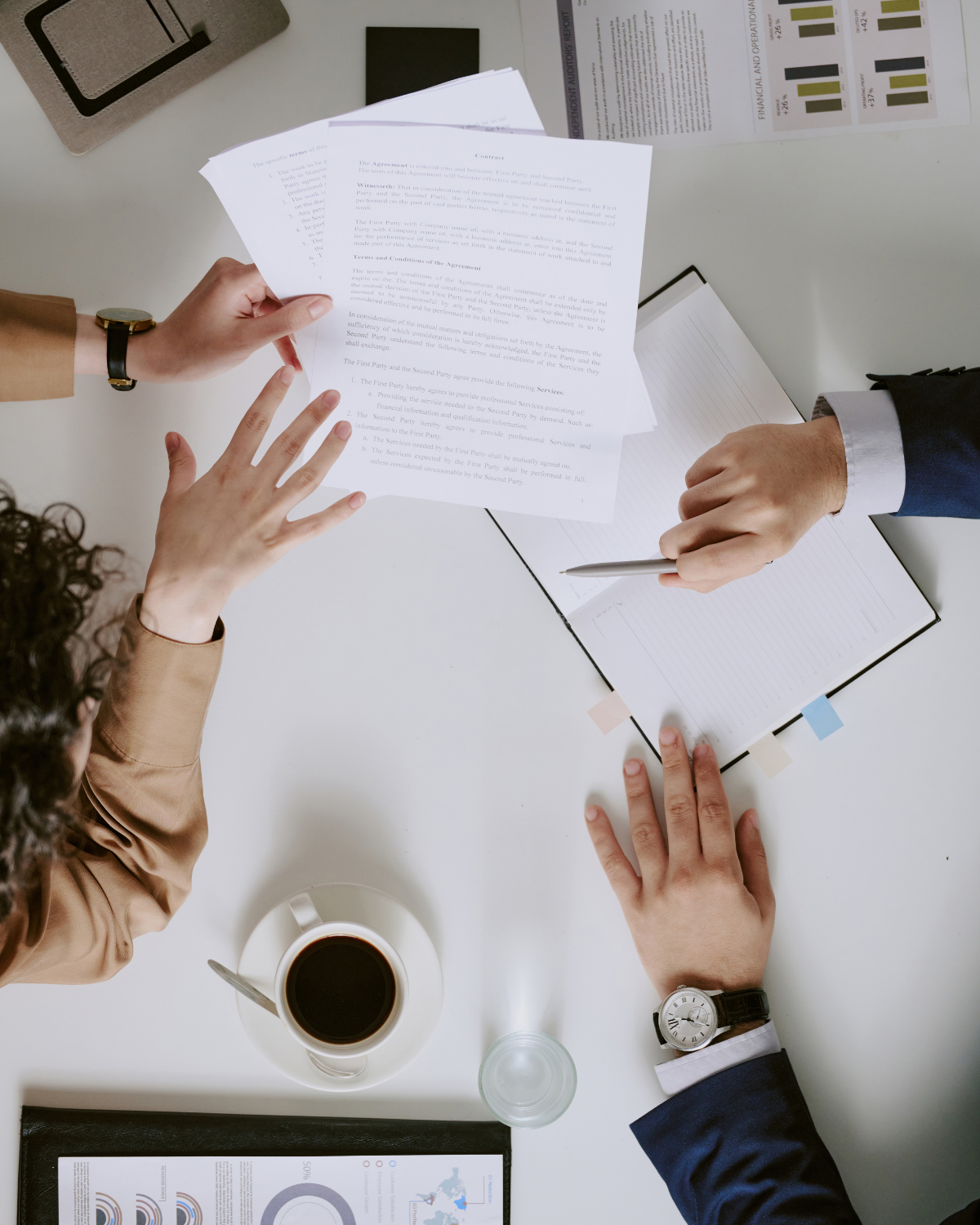 image of documents, notebook, coffee on a desk with a person's hands either side