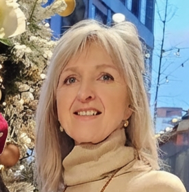 Ältere Frau mit blondem Haar, beige Mantel, in einer festlichen Umgebung mit Weihnachtsdekoration