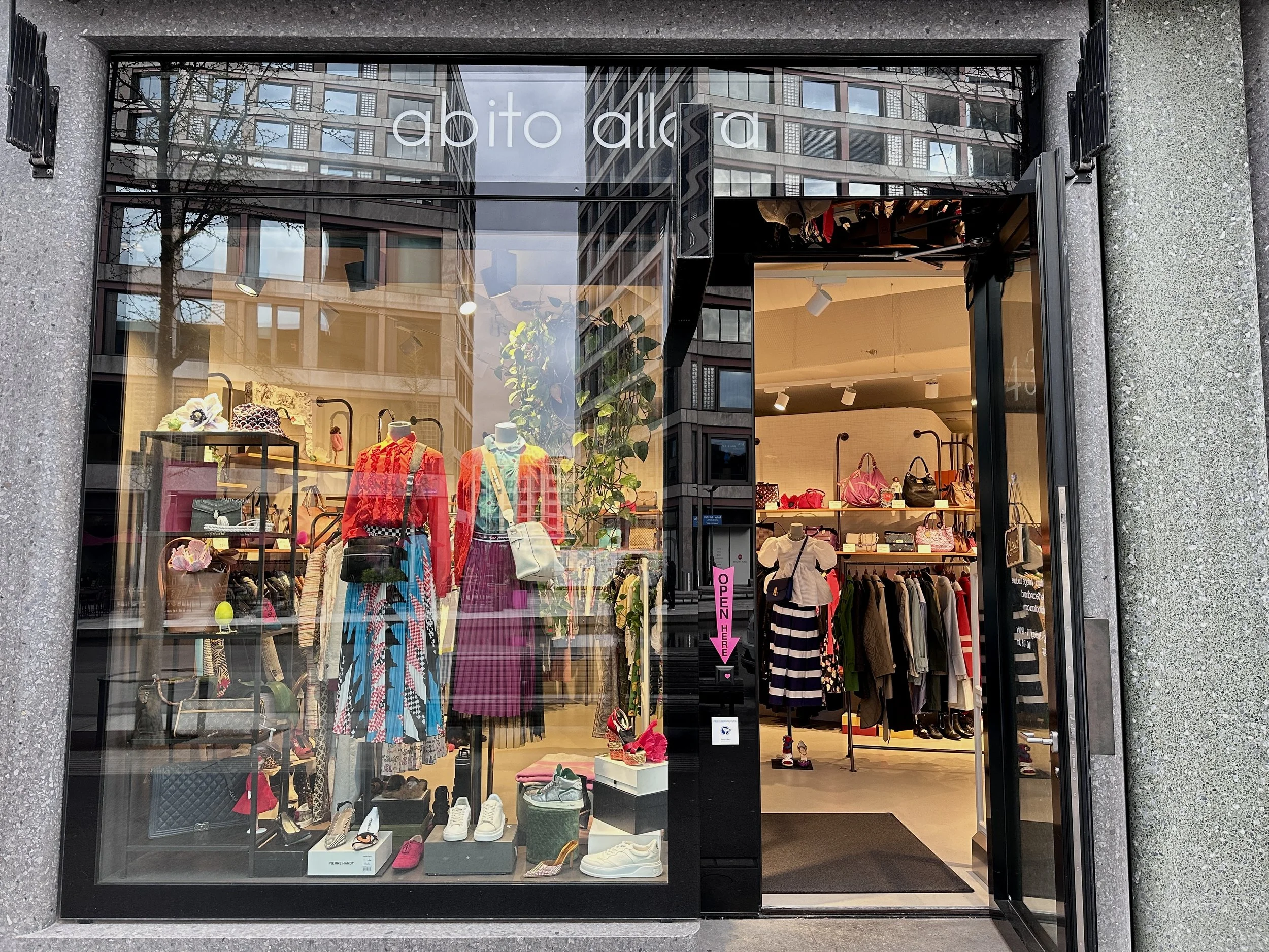 Schaufenster eines Modegeschäfts mit Kleidung, Schuhen und Accessoires, im Inneren sind Kleider, Taschen und Schuhe sichtbar.