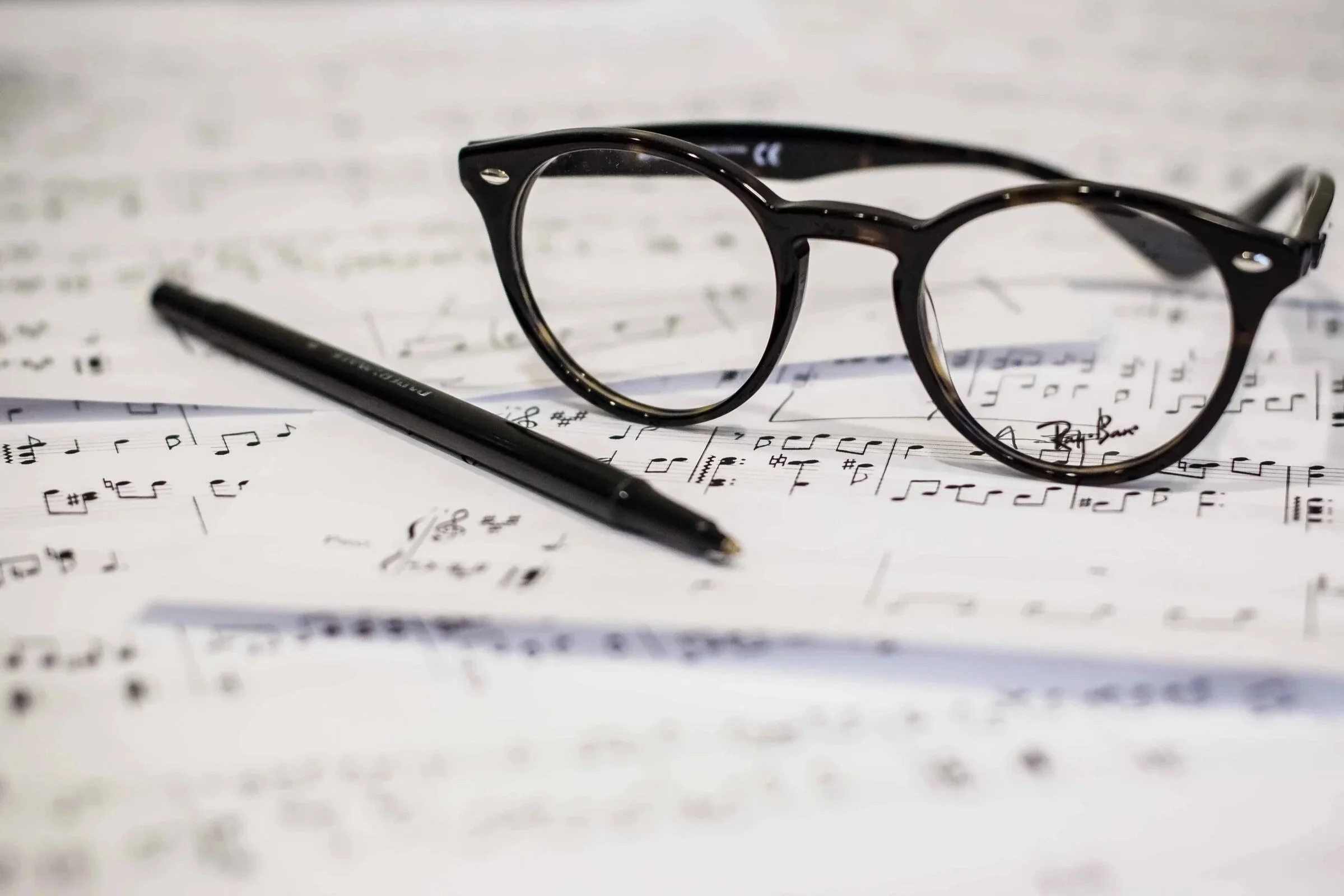 A pair of black eyeglasses and a black pen resting on sheets of musical notation.