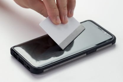 Black phone with hand over top holding a squeegee to remove bubbles from an installed screen protector on a mobile device