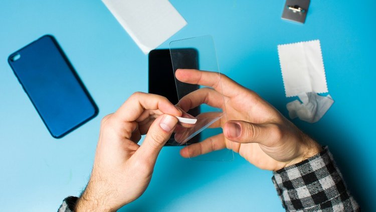 Hands putting a Screen protector on a smart phone with microfibre cloths on desk