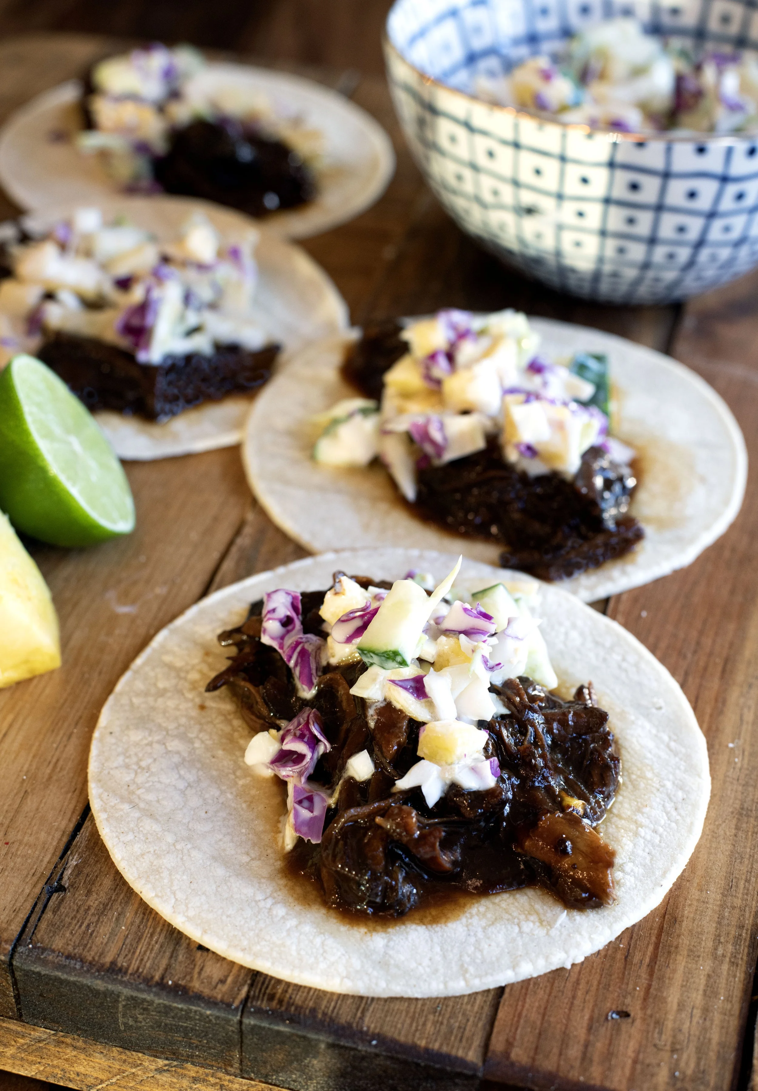 huli huli javelina sitting on a warm corn tortilla topped with a creamy green and purple cabbage slaw with pineapple and cucumbers