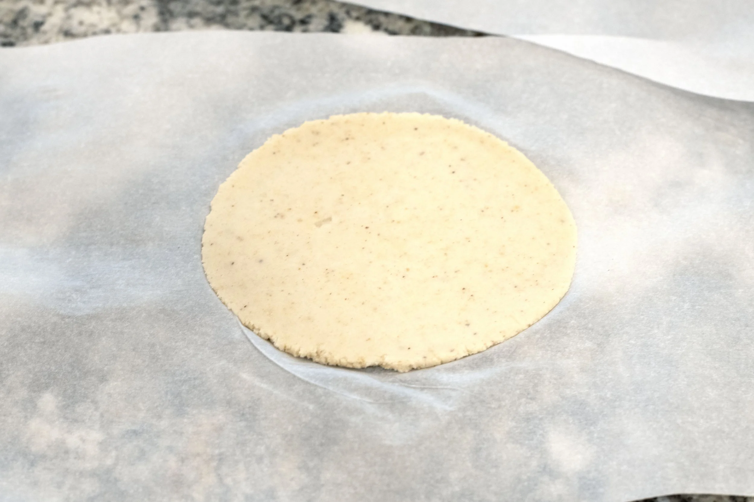 Flat pressed tortilla shell on a piece of parchment paper