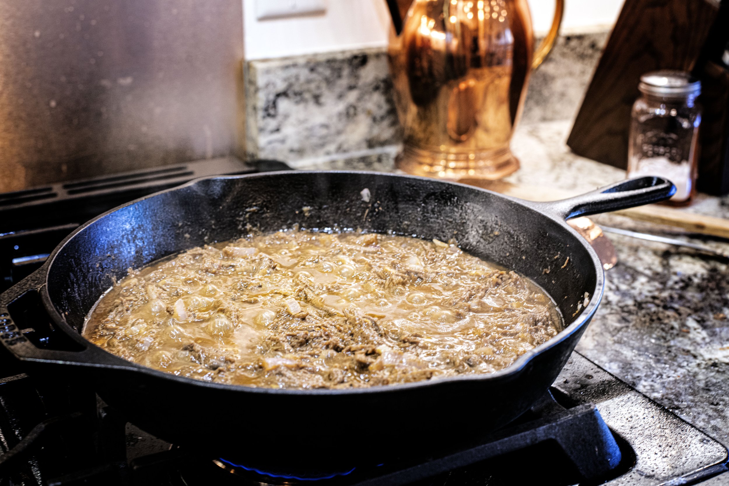 Cast iron skillet sits on the stove simmering apricot venison taco meat