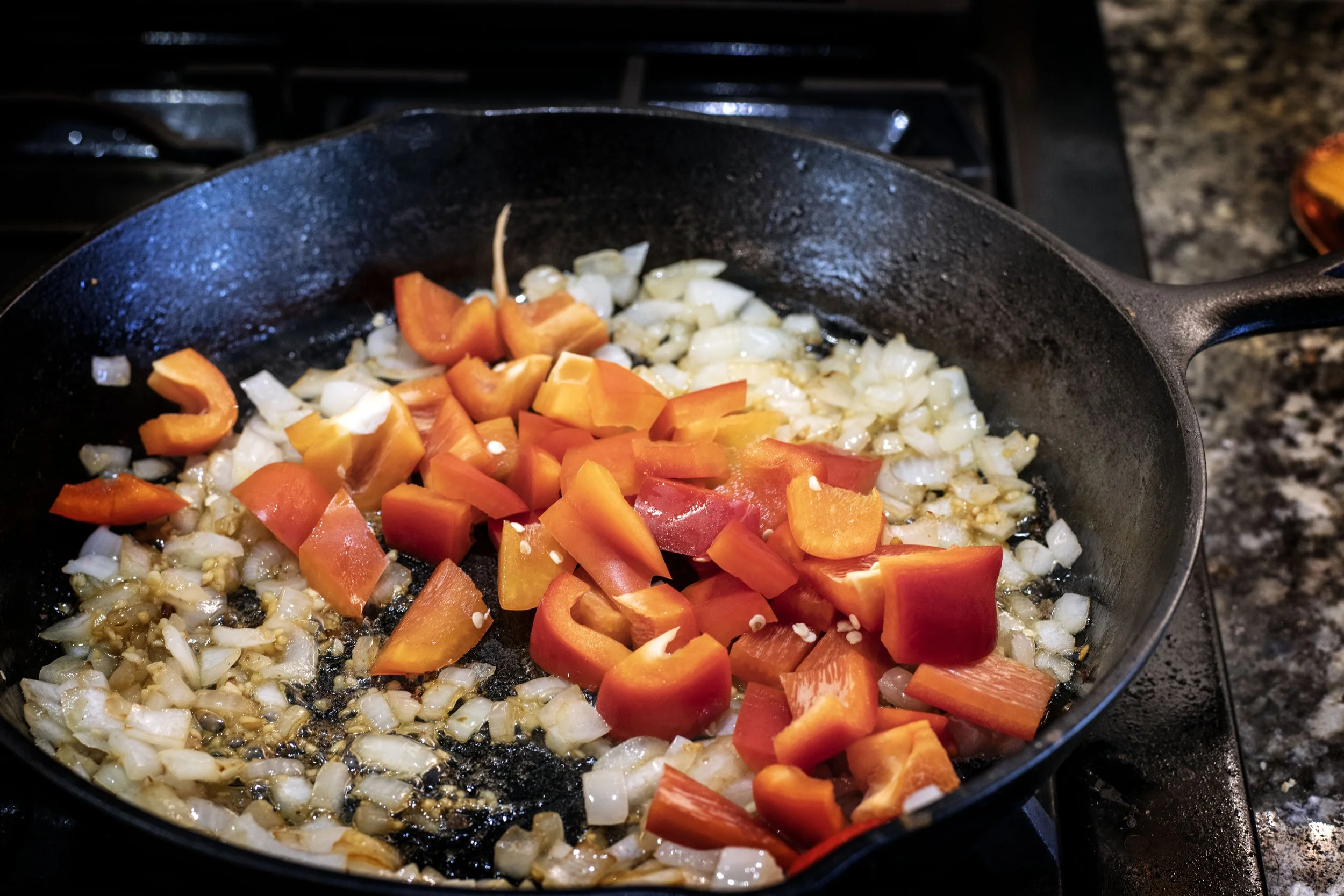 softened white onions and red bell peppers cooking in a heavy cast iron skillet