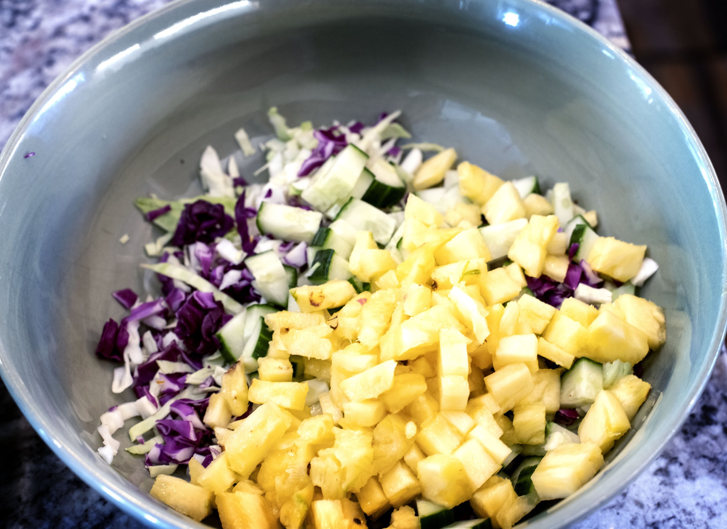 Bowl with shredded green and purple cabbage, pineapple tidbits, and diced cucumber