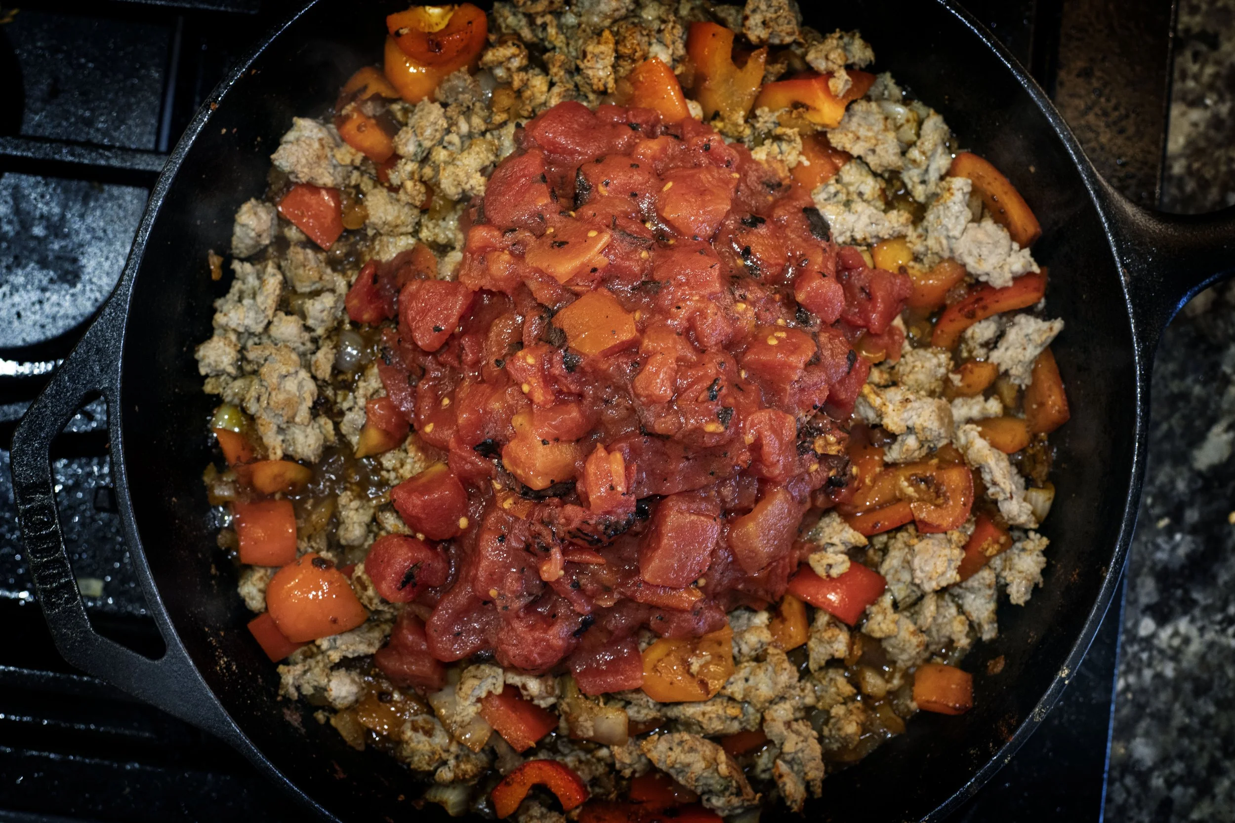 fire-roasted tomatoes on top of ground pheasant in cast iron skillet