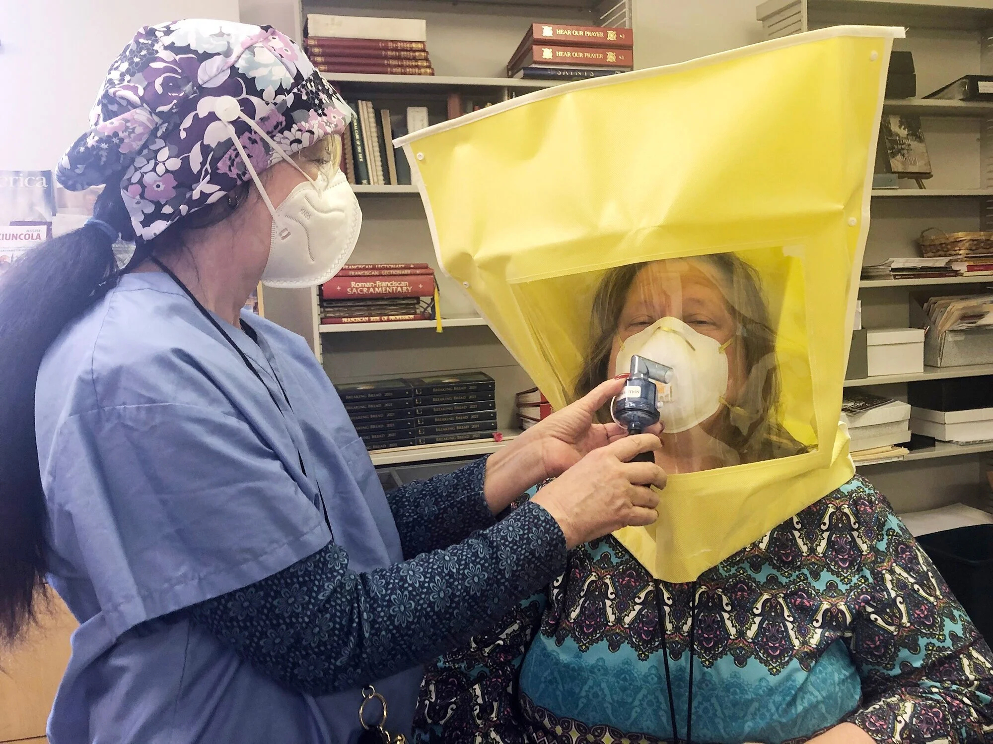A healthcare professional from Allegheny Health Network uses a special hood to fit Nicole Buchlmayer, communications coordinator, for a N-94 face mask.