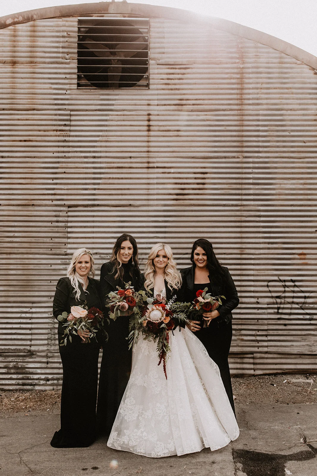 Bride and bridesmaids with leather jackets and deep red bouquets at industrial warehouse wedding 