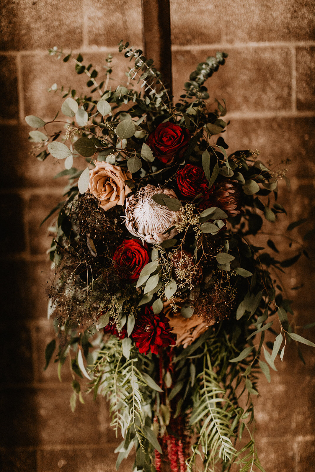 Ceremony arch wedding flowers with King Protea, red roses, dahlias and brown roses