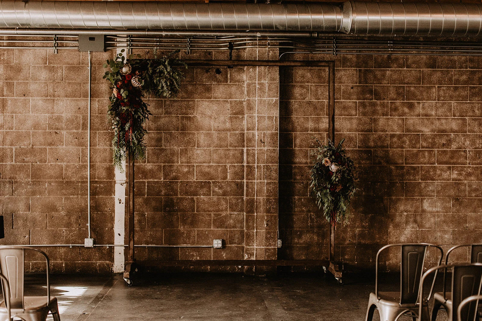 Metal wedding ceremony arch and asymmetrical dark moody flowers in pink and red and brown