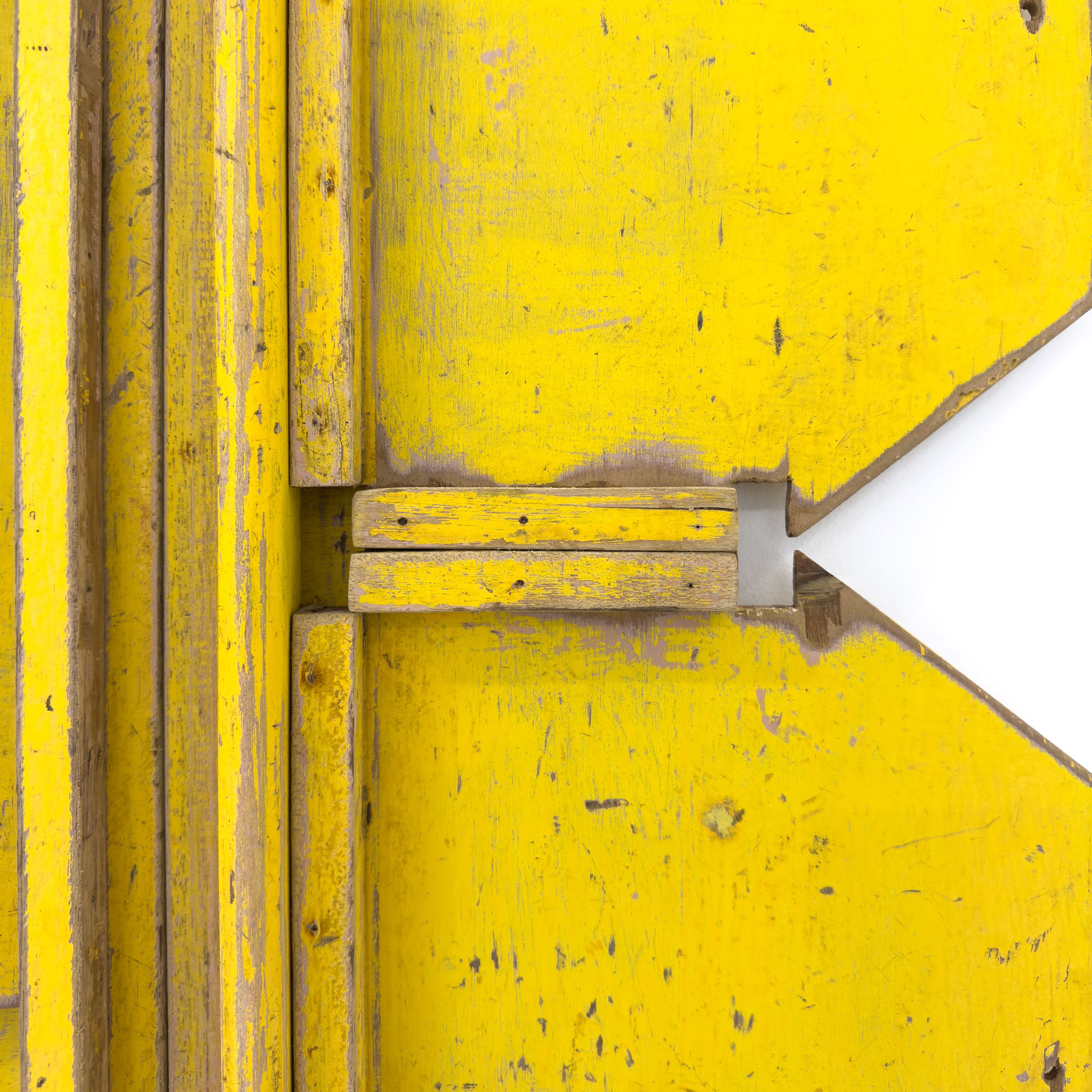 Bright yellow, distressed wooden panel with geometric cutouts and visible wood grain. The texture conveys a rustic and artistic vibe.