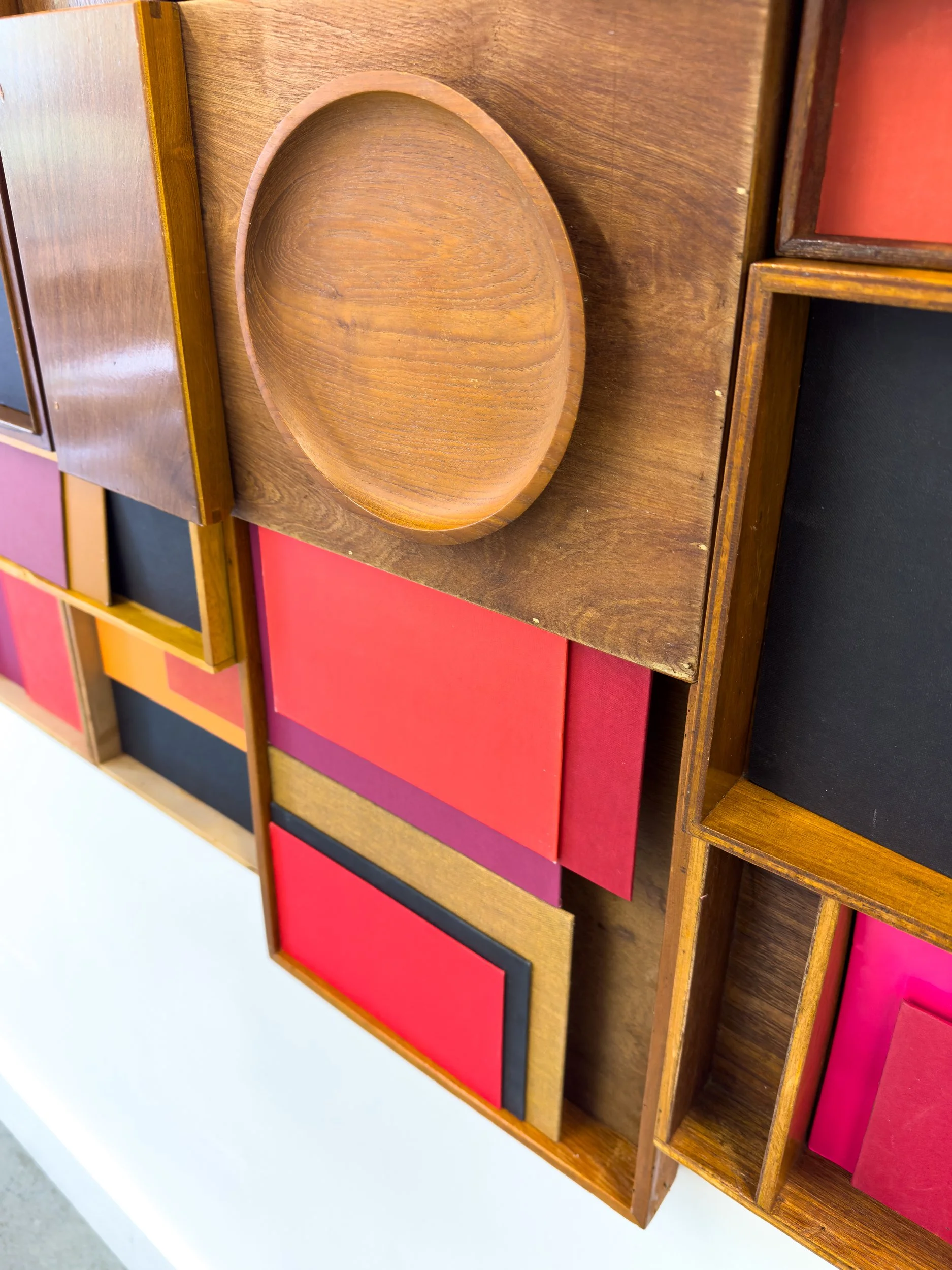 Wall art featuring wooden panels and colorful rectangles in red, pink, and black, arranged in a geometric pattern with a modern, vibrant feel.