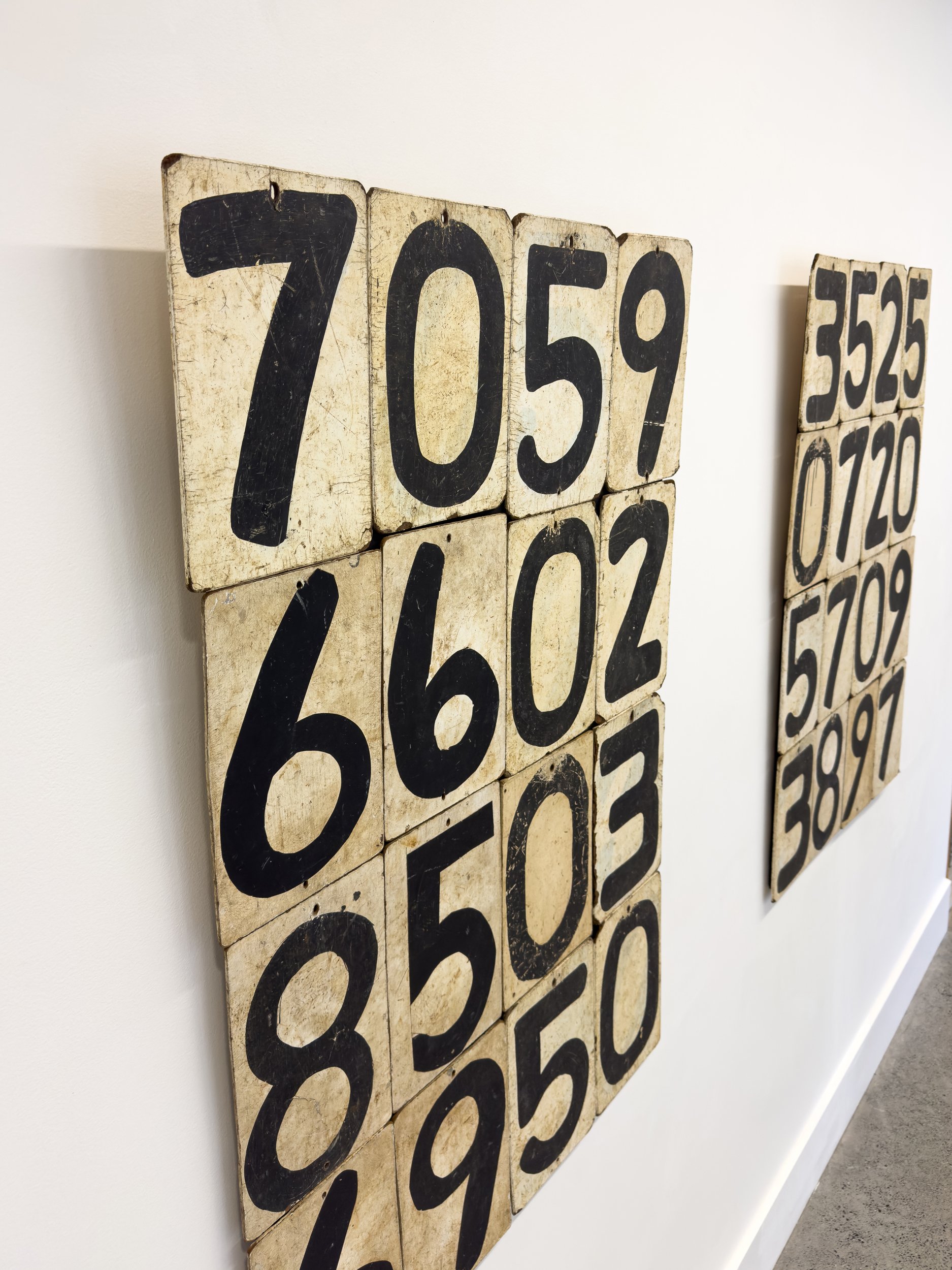 Vintage number boards hang on a white wall. The foreground board shows large black numbers on a weathered white background, evoking a nostalgic feel.
