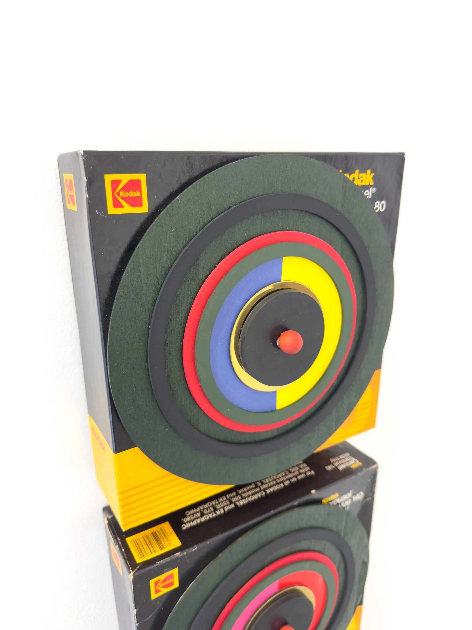 Close-up of two stacked Kodak boxes with retro circular designs featuring bold red, blue, yellow, and black concentric circles. The design evokes a vintage feel.
