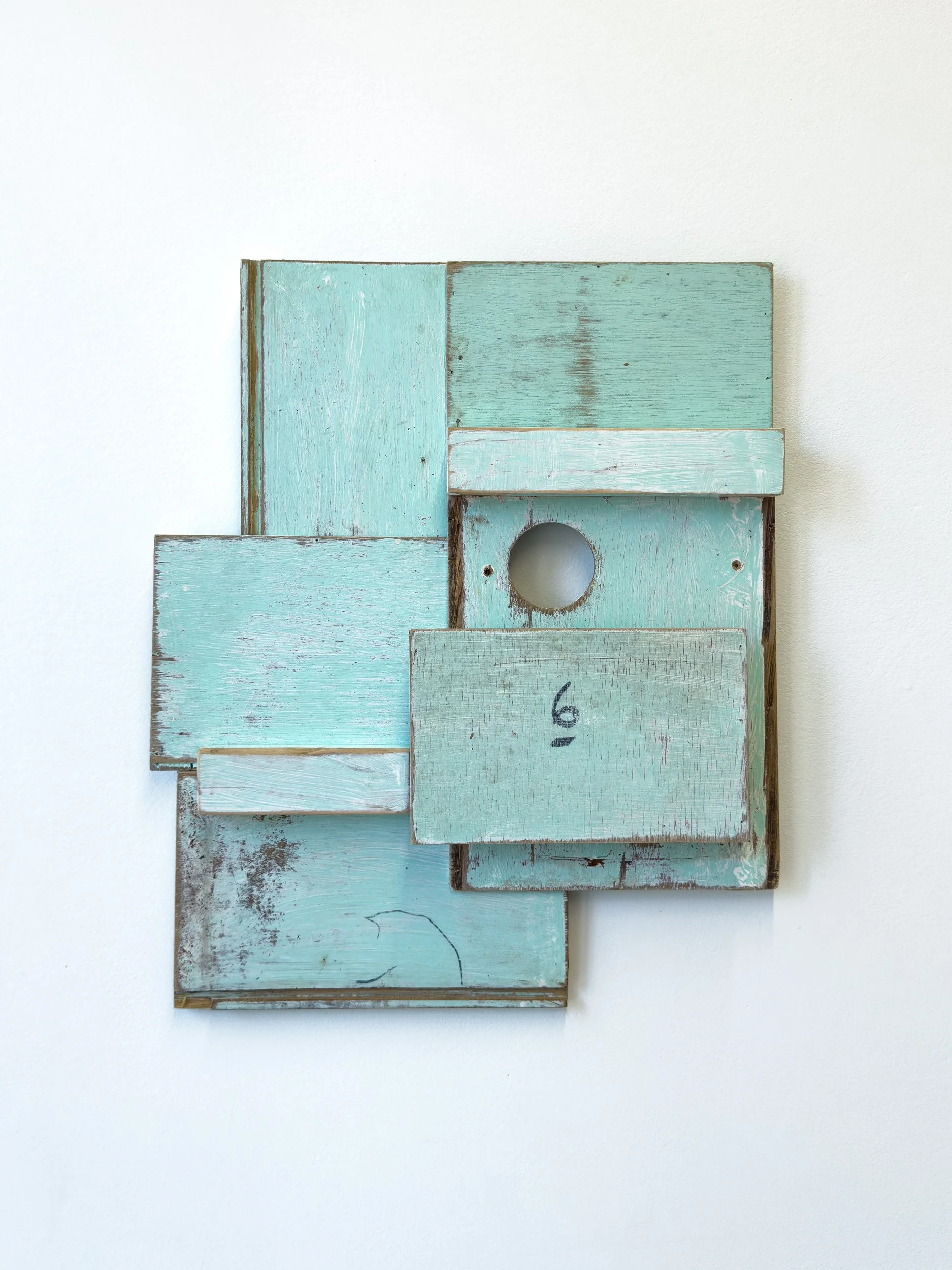 Abstract art piece featuring layered, weathered turquoise wooden panels with a small circular cutout. A rough, rustic aesthetic and number "6" are visible.