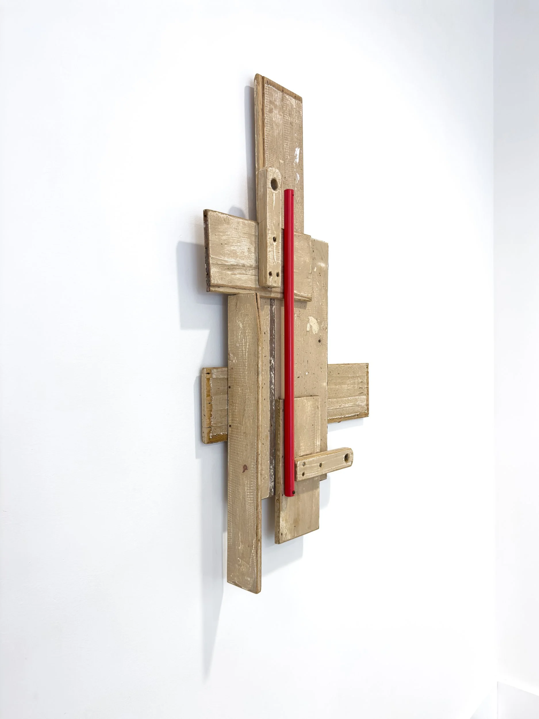 A geometric wall sculpture made of overlapping wooden planks with a vertical red accent. Set against a white wall, it conveys a modern, minimalist tone.