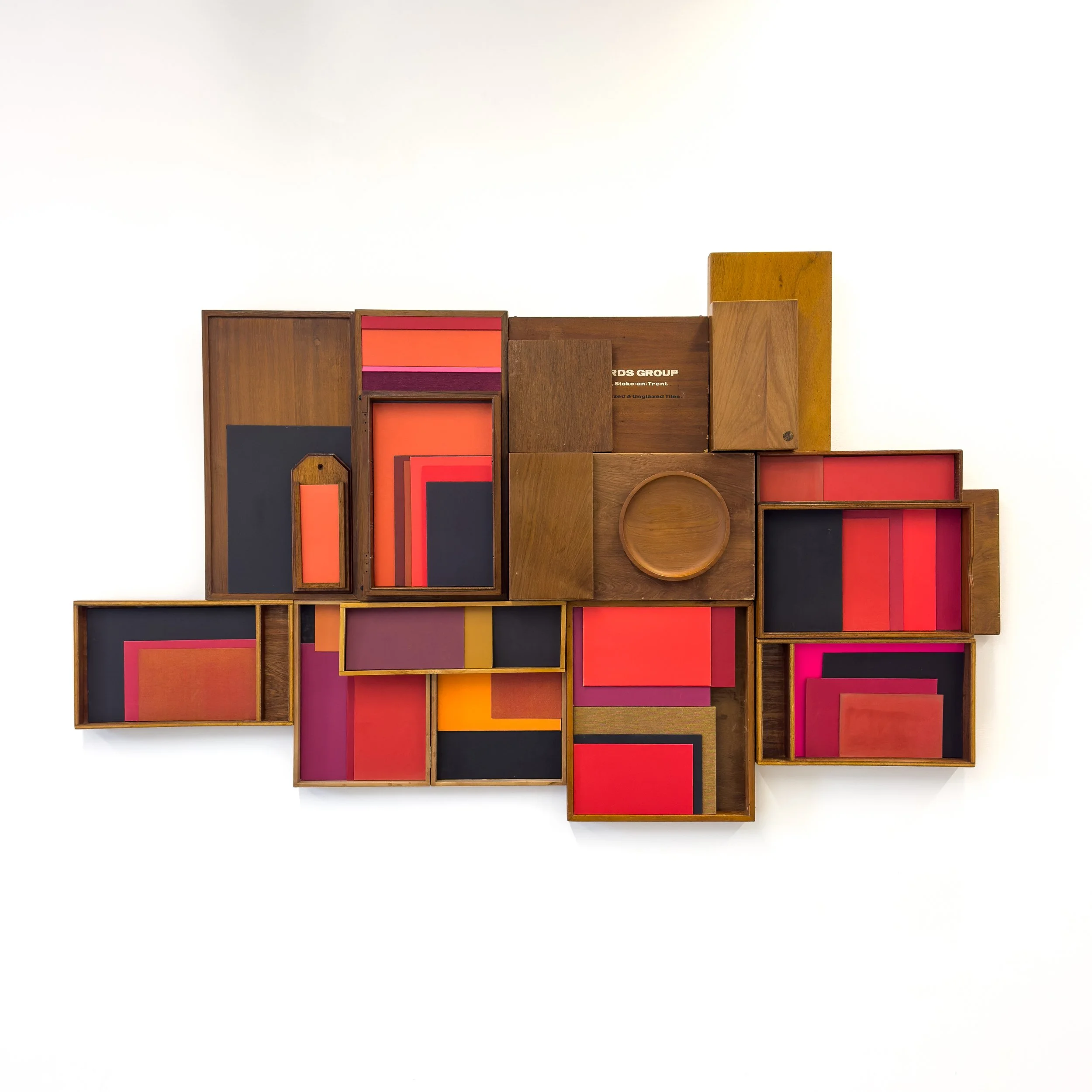 Abstract wall art made of wooden boxes filled with red, orange, and black panels. Arranged in a mosaic, it conveys a modern, dynamic feel.