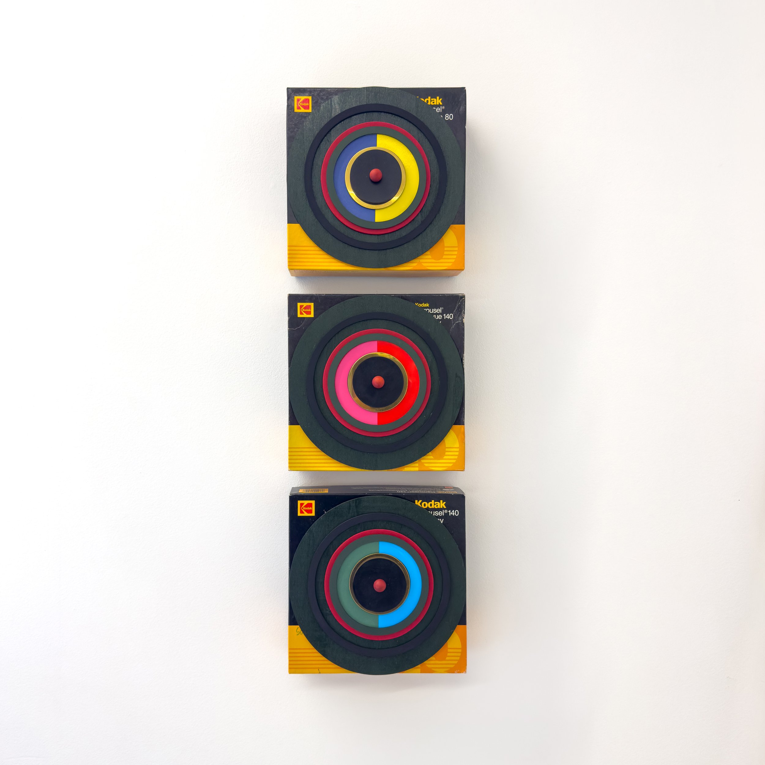 Three colorful, concentric circle artworks mounted vertically on a wall. Each piece is on a Kodak reel box, featuring vibrant reds, blues, and yellows.
