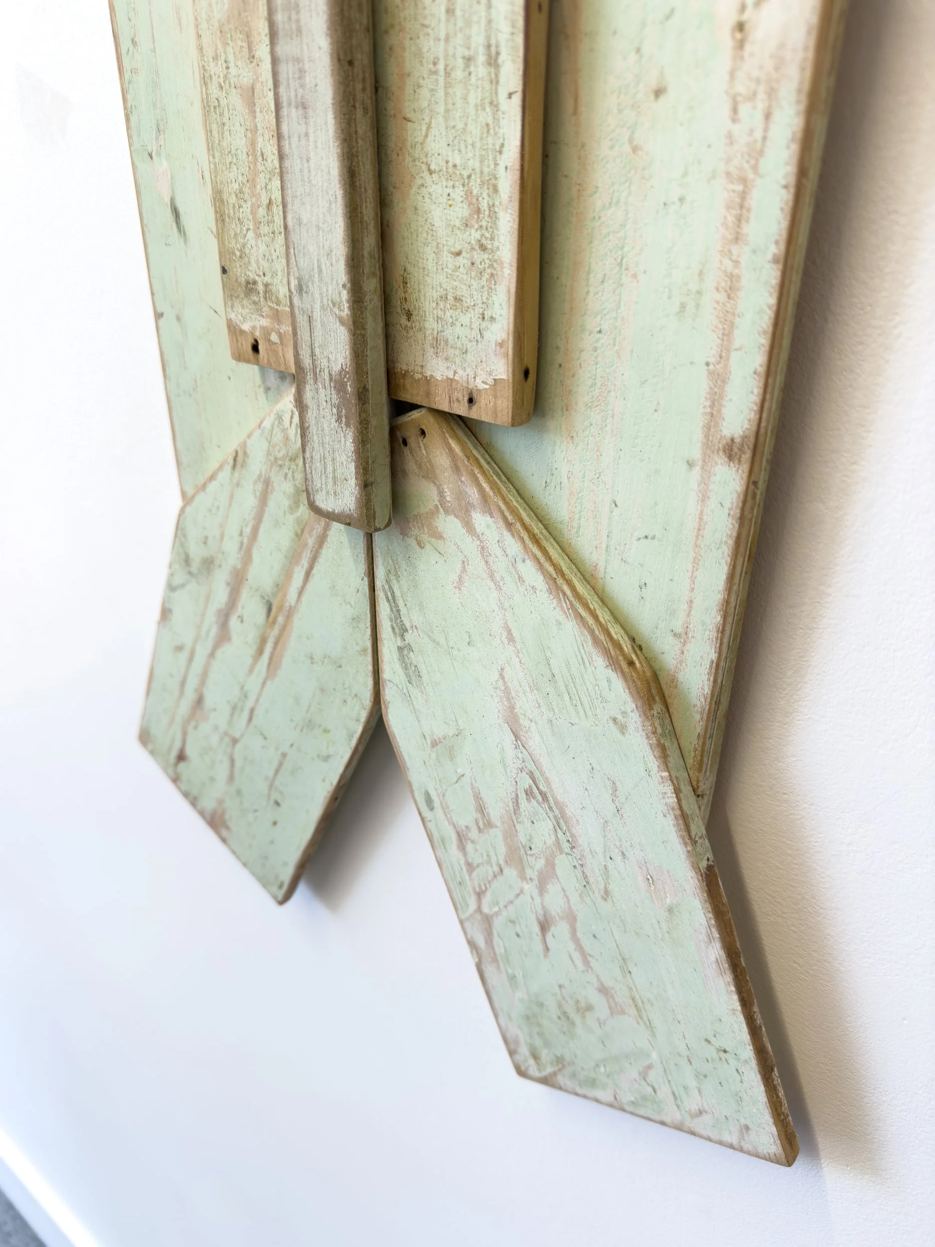 A close-up of a distressed wooden surface shaped like two overlapping arrows pointing downwards. The wood is painted mint green with visible worn patches.