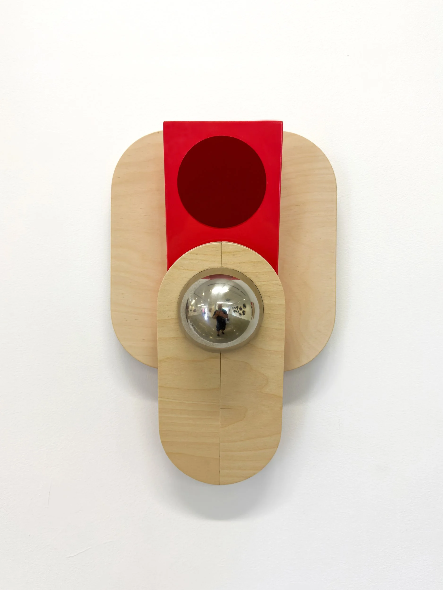 Abstract wall sculpture with layered wooden shapes, featuring a metallic sphere and a red rectangle. Minimalist design with a modern, artistic tone.