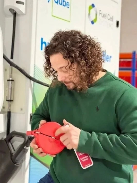 Man with short curly hair and a slight beard wearing a black shirt, looking at the camera.