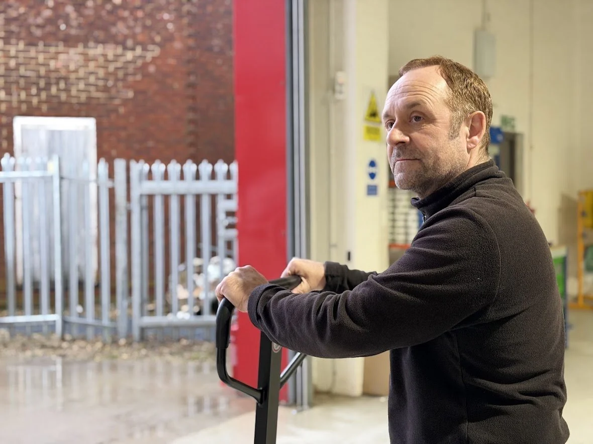 Man organizing plastic bins and checking a packaged item on a shelf in a warehouse.