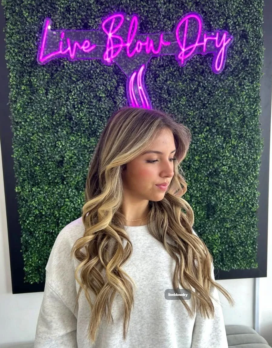 Voluminous blonde blowout under the pink Live Blow Dry neon sign in Pinecrest