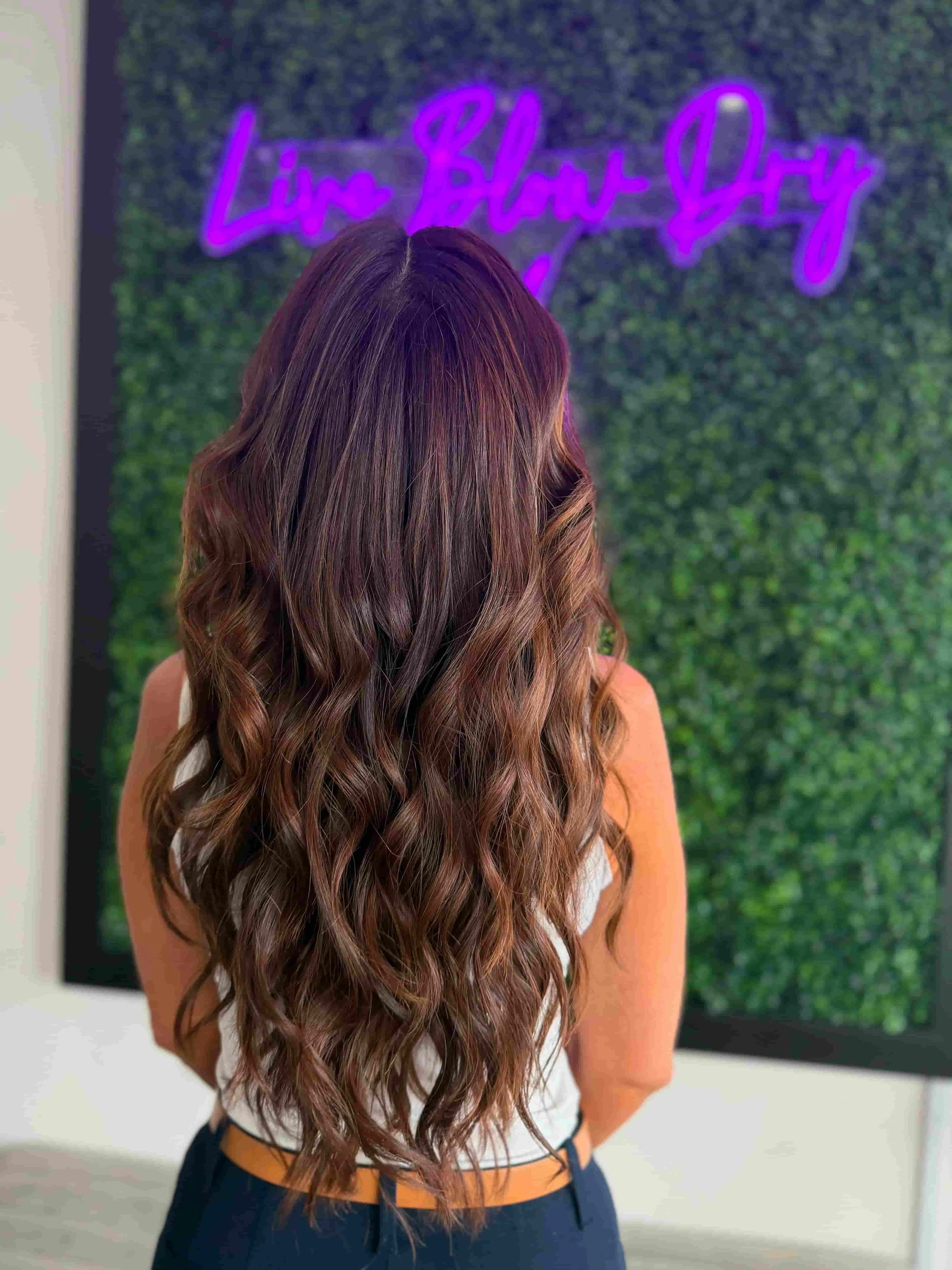 Long wavy brunette blowout in front of the Live Blow Dry neon sign