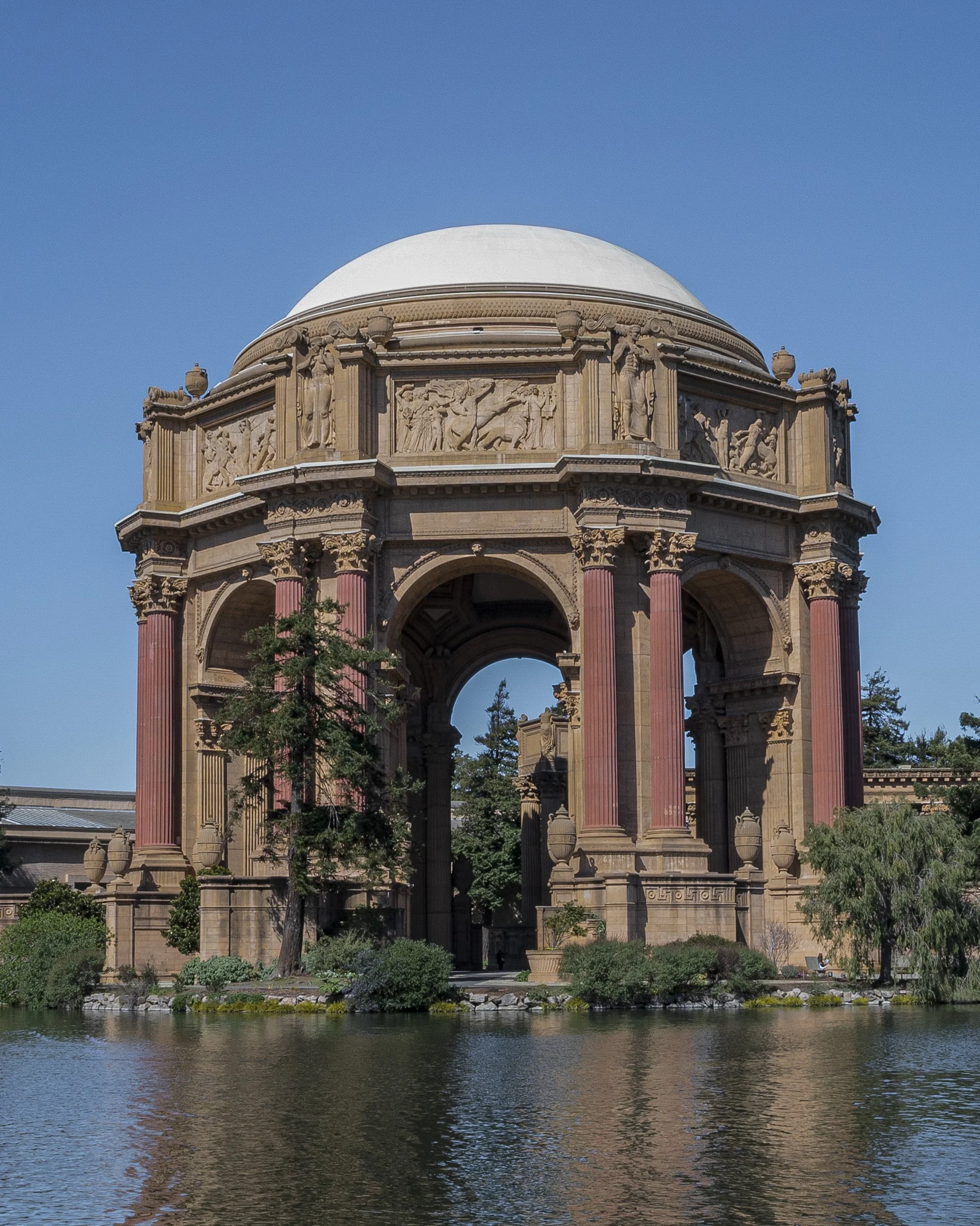 The Palace of Fine Arts in San Francisco, California, featuring an ornate, classical-style architectural structure with a large dome, columns, and decorative sculptures, reflected in a pond at its base.