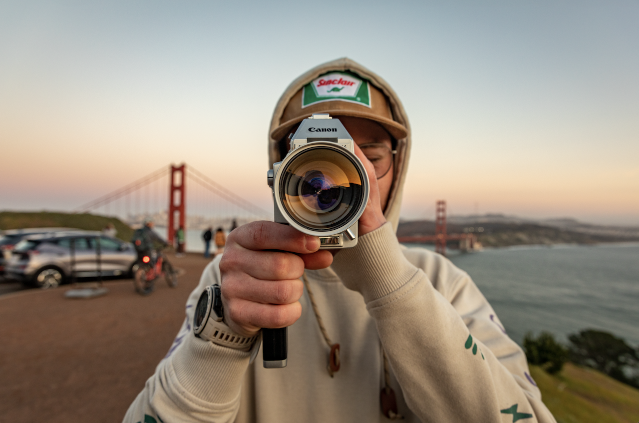 Person holding a camera with the Golden Gate Bridge in the background at sunset.
