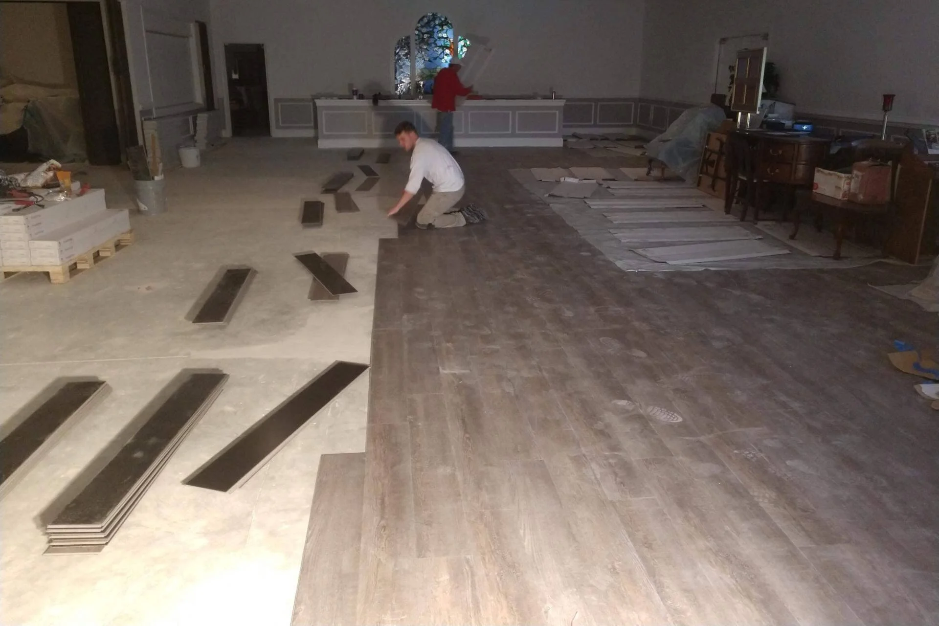 Two flooring contractors installing rustic gray click Luxury Vinyl Plank (LVP) inside a large banquet hall of a hotel.