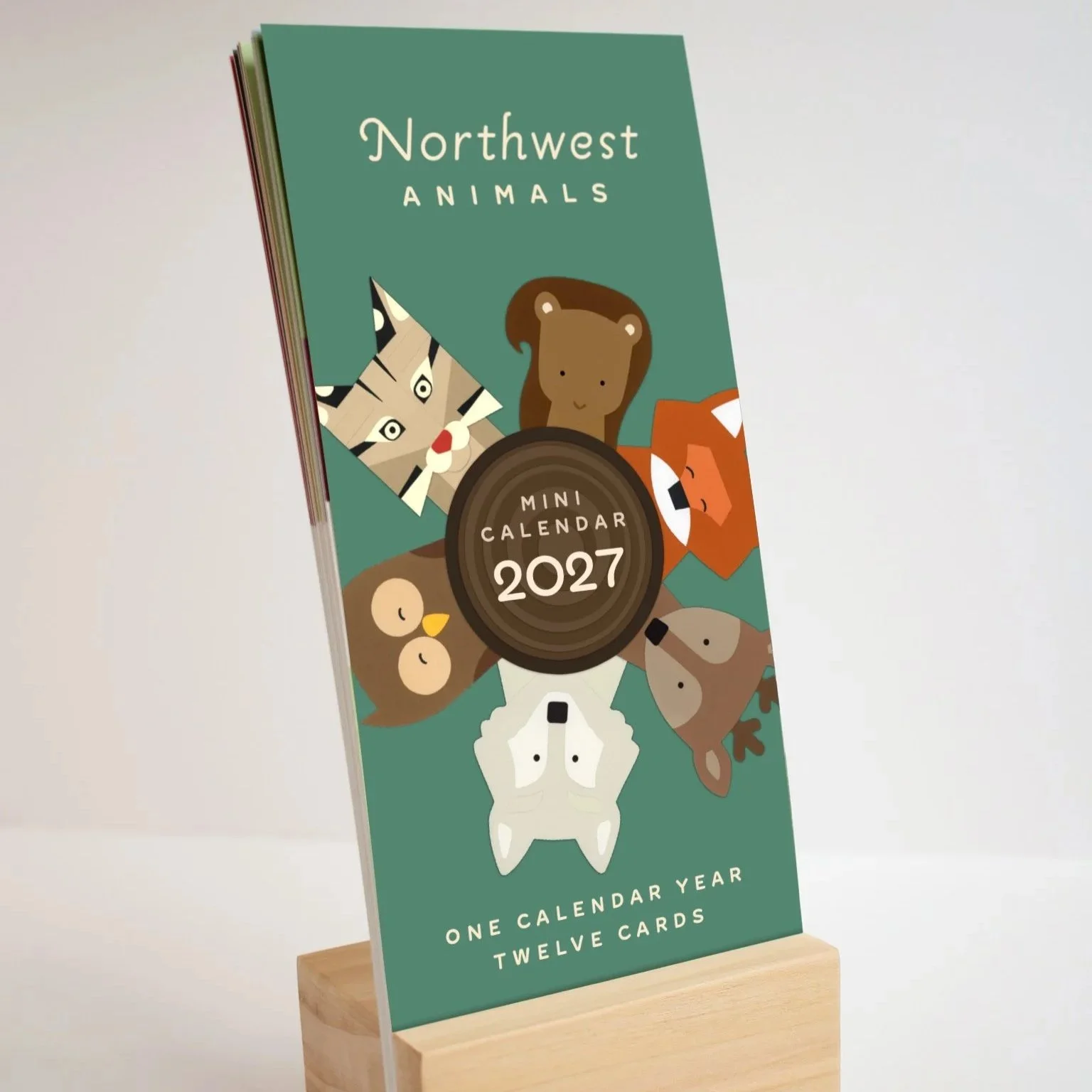 Adorable artist-made desk calendar featuring paper artwork by Allison Palmer: Northwest Animals in 2027 featured on their own month card, includes a handmade wooden stand to feature the calendar pages all year long.