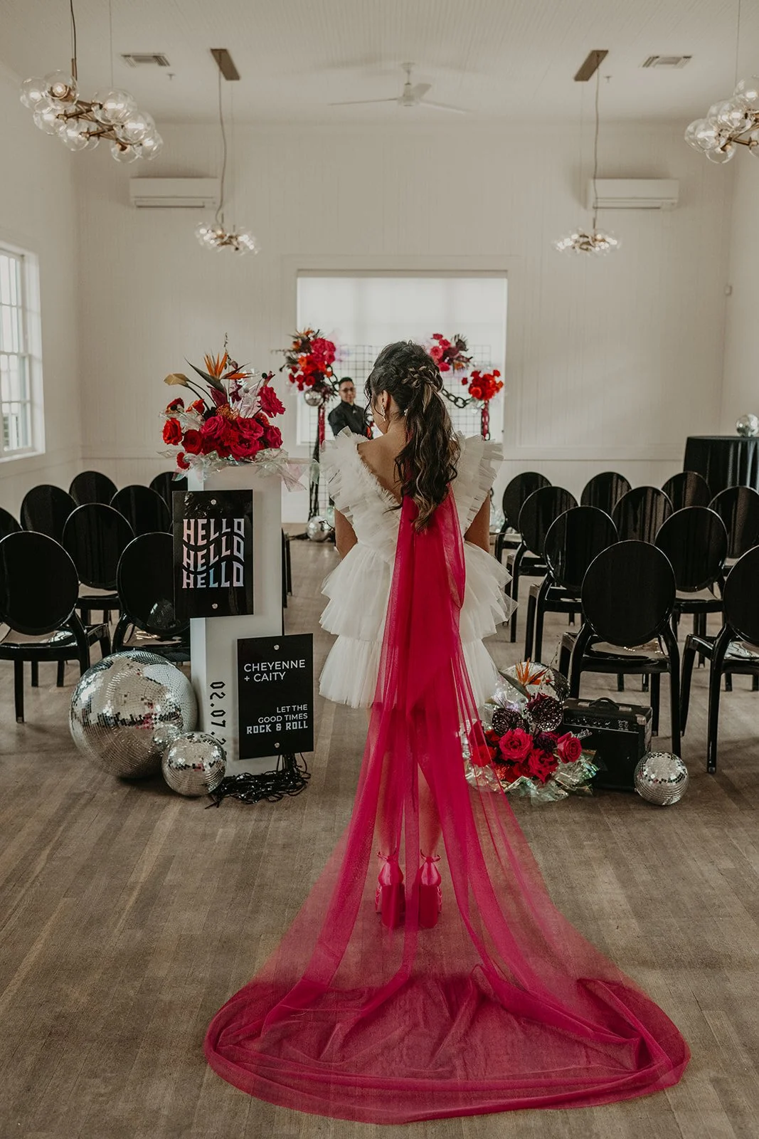 Bride facing away, about to walk down the aisle as her rock n roll inspired wedding. She has a hot pink veil and a bridal ponytail.