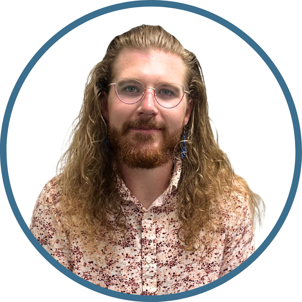 Portrait of a therapist with long, curly hair, a beard, and glasses, wearing a floral patterned shirt, against a white background.